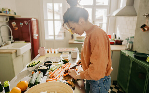 Junge Frau steht in der Küche und schneidet Gemüse in Streifen.