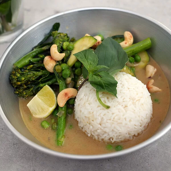 Grünes Gemüsecurry mit Zucchini nach einem Rezept von Felicitas Then, angerichtet auf einem hellgrauen Teller, garniert mit Thai-Basilikum und gerösteten Cashewkernen.