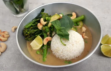 Grünes Gemüsecurry mit Zucchini nach einem Rezept von Felicitas Then, angerichtet auf einem hellgrauen Teller, garniert mit Thai-Basilikum und gerösteten Cashewkernen.