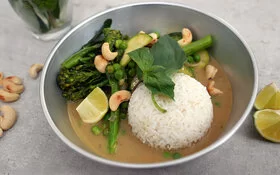 Grünes Gemüsecurry mit Zucchini nach einem Rezept von Felicitas Then, angerichtet auf einem hellgrauen Teller, garniert mit Thai-Basilikum und gerösteten Cashewkernen.