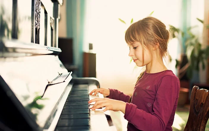 Ein Mädchen sitzt an einem Klavier und greift mit beiden Händen in die Tasten.