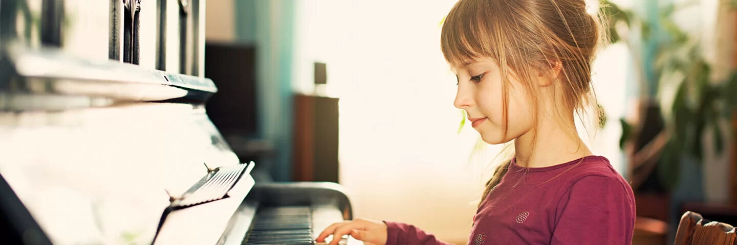 Ein Mädchen sitzt an einem Klavier und greift mit beiden Händen in die Tasten.
