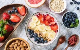 Gesundes Frühstück, bestehend aus einer Smoothie Bowl mit Blau- und Erdbeeren, Bananen und Nüssen angereichert, daneben Mandeln in einer Schale.