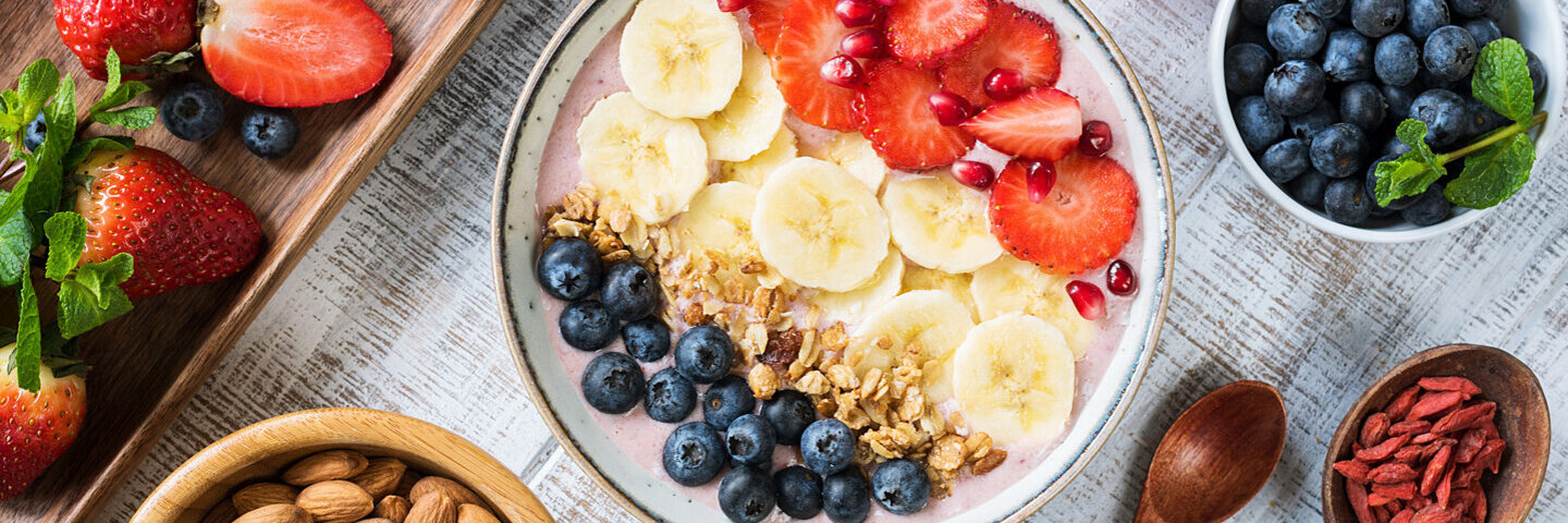 Gesundes Frühstück, bestehend aus einer Smoothie Bowl mit Blau- und Erdbeeren, Bananen und Nüssen angereichert, daneben Mandeln in einer Schale.