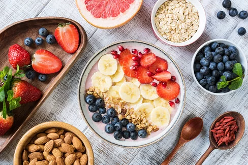 Gesundes Frühstück, bestehend aus einer Smoothie Bowl mit Blau- und Erdbeeren, Bananen und Nüssen angereichert, daneben Mandeln in einer Schale.