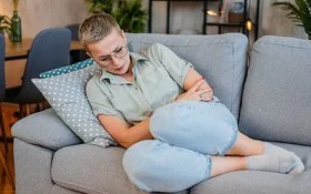 Eine junge Frau liegt mit Schmerzen auf dem Sofa.