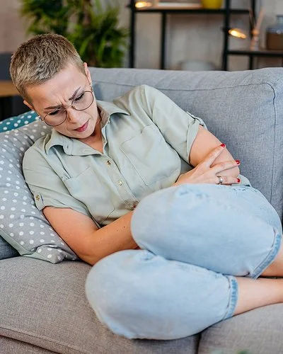 Eine junge Frau liegt mit Schmerzen auf dem Sofa.