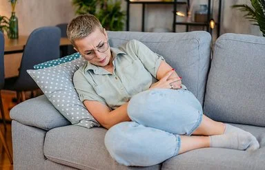 Eine junge Frau liegt mit Schmerzen auf dem Sofa.