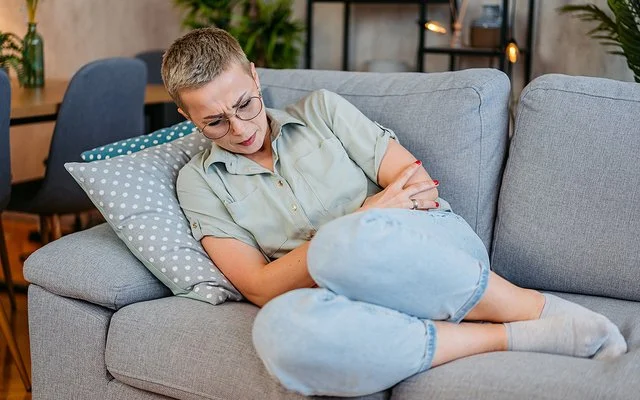 Eine junge Frau liegt mit Schmerzen auf dem Sofa.