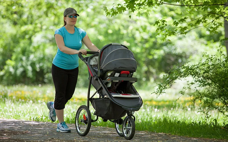 Frau geht mit ihrem Neugeborenen im Kinderwagen spazieren.