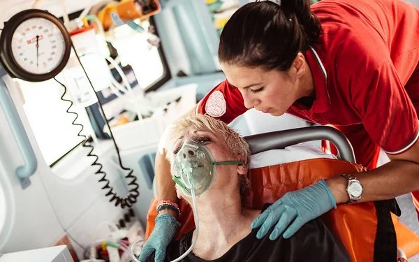Eine Sanitäterin kümmert sich im Krankenwagen um eine Frau, die eine Atemmaske trägt.