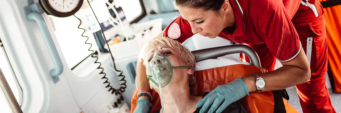 Eine Sanitäterin kümmert sich im Krankenwagen um eine Frau, die eine Atemmaske trägt.