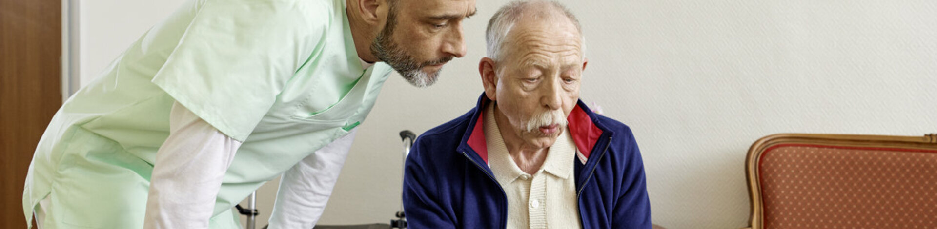 Eine Pflegekraft hilft einem älteren Mann im Altersheim beim Ausfüllen eines Formulares.