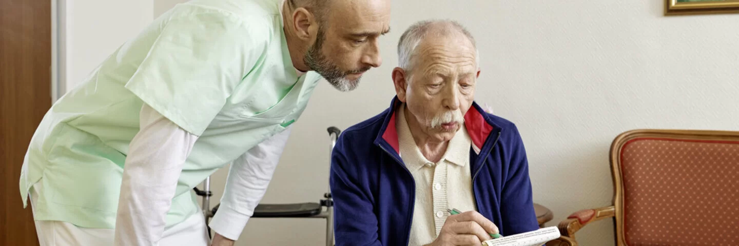 Eine Pflegekraft hilft einem älteren Mann im Altersheim beim Ausfüllen eines Formulares.