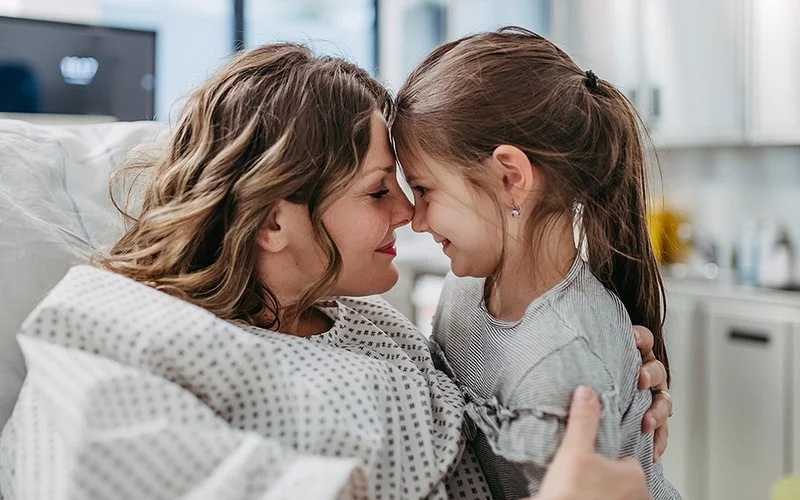 Eine Mutter liegt in einem Krankenhausbett und umarmt ihre kleine Tochter.