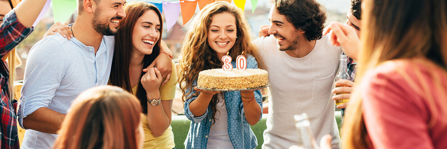 Mehrere Personen stehen im Kreis zusammen und feiern einen 30. Geburtstag mit einer Geburtstagstorte.