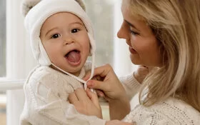 Babys richtig anziehen - Mutter setzt ihrem Kind eine Mütze auf.