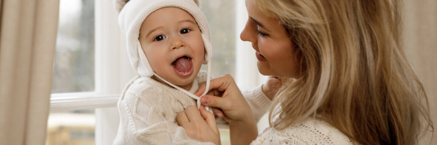 Babys richtig anziehen - Mutter setzt ihrem Kind eine Mütze auf.