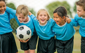 Fünf Fußball spielende Kinder umarmen sich und lachen.