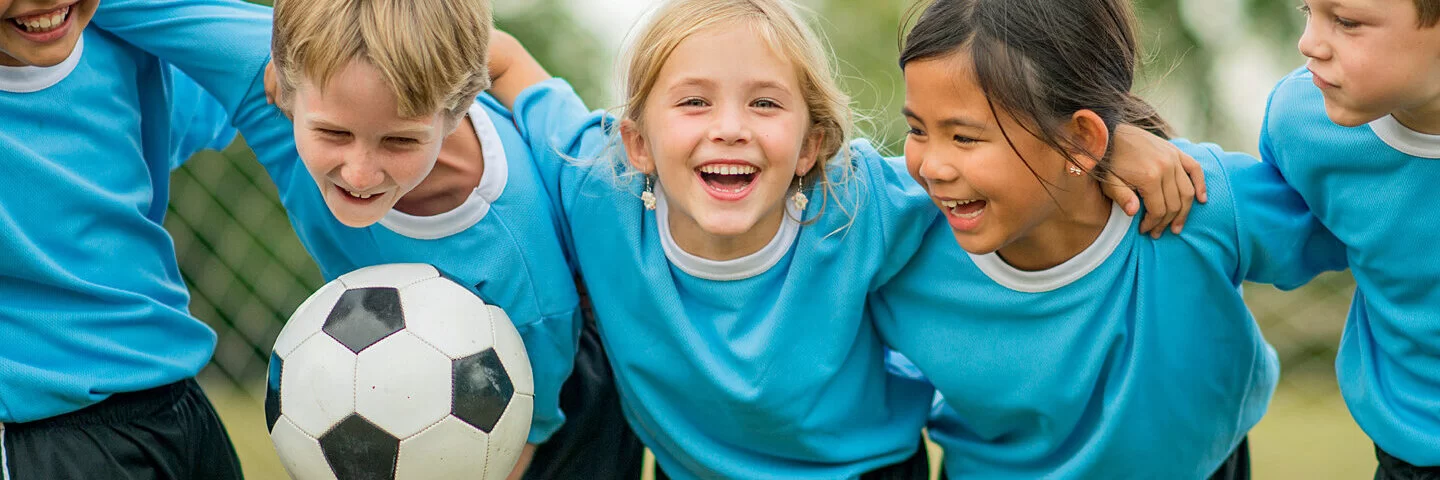 Fünf Fußball spielende Kinder umarmen sich und lachen.