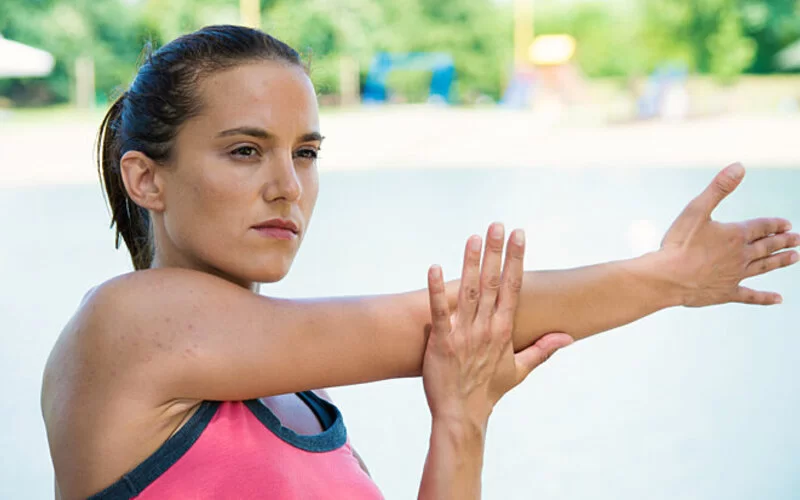 Frau behandelt ihren Tennisarm mit Dehnübungen.