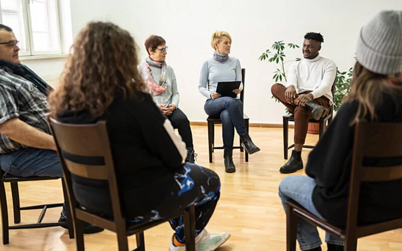 Eine Selbsthilfegruppe für Menschen mit Trauma sitzt in einem Stuhlkreis.