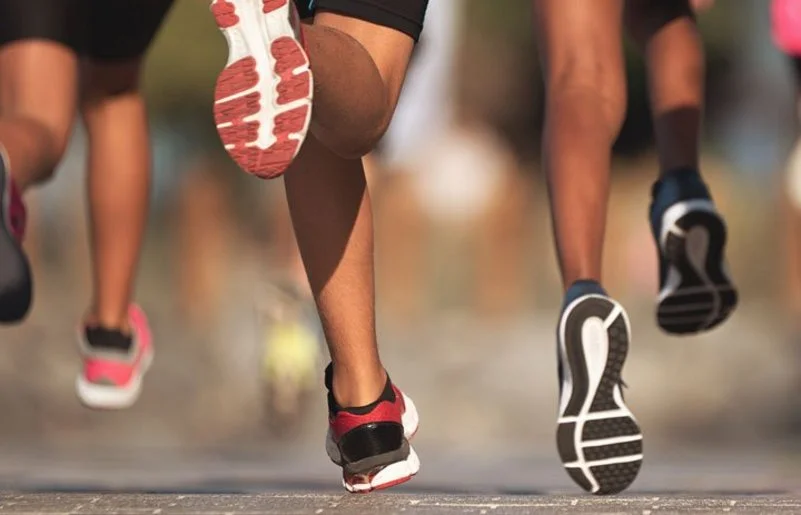 Die Füße von einer Laufgruppe, die auf einer Straße läuft.