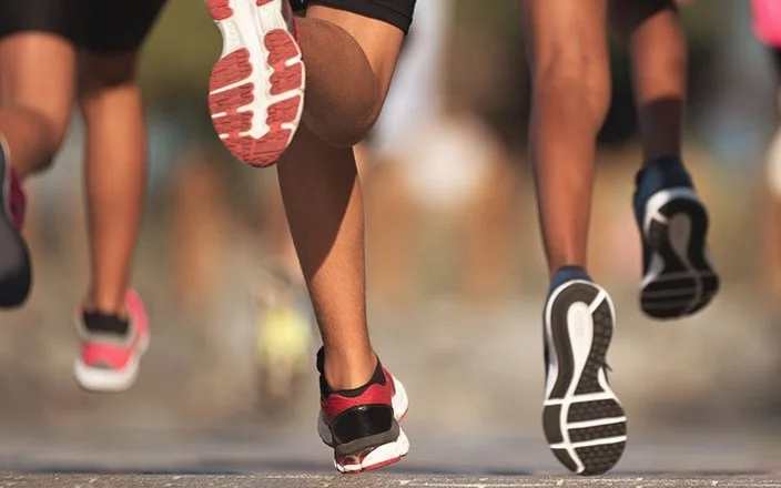 Die Füße von einer Laufgruppe, die auf einer Straße läuft.