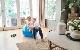 Seniorin trainiert ihr Gleichgewicht mit Übungen auf einem Gymnastikball.