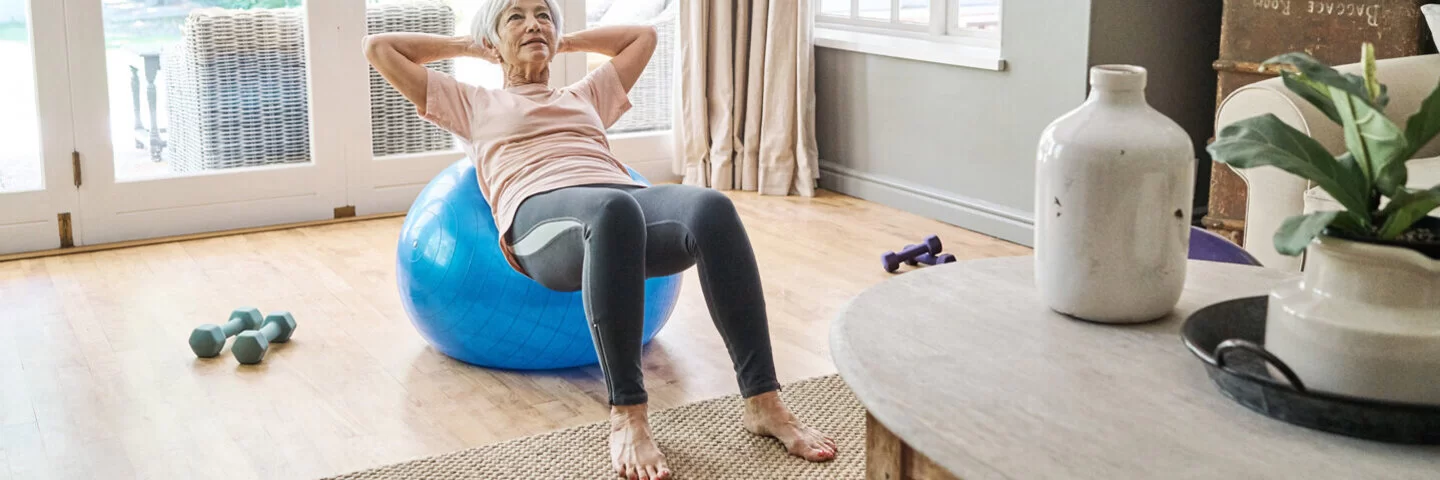 Seniorin trainiert ihr Gleichgewicht mit Übungen auf einem Gymnastikball.