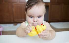 Ein Baby schielt und schaut zwei gelbe Gummienten an.