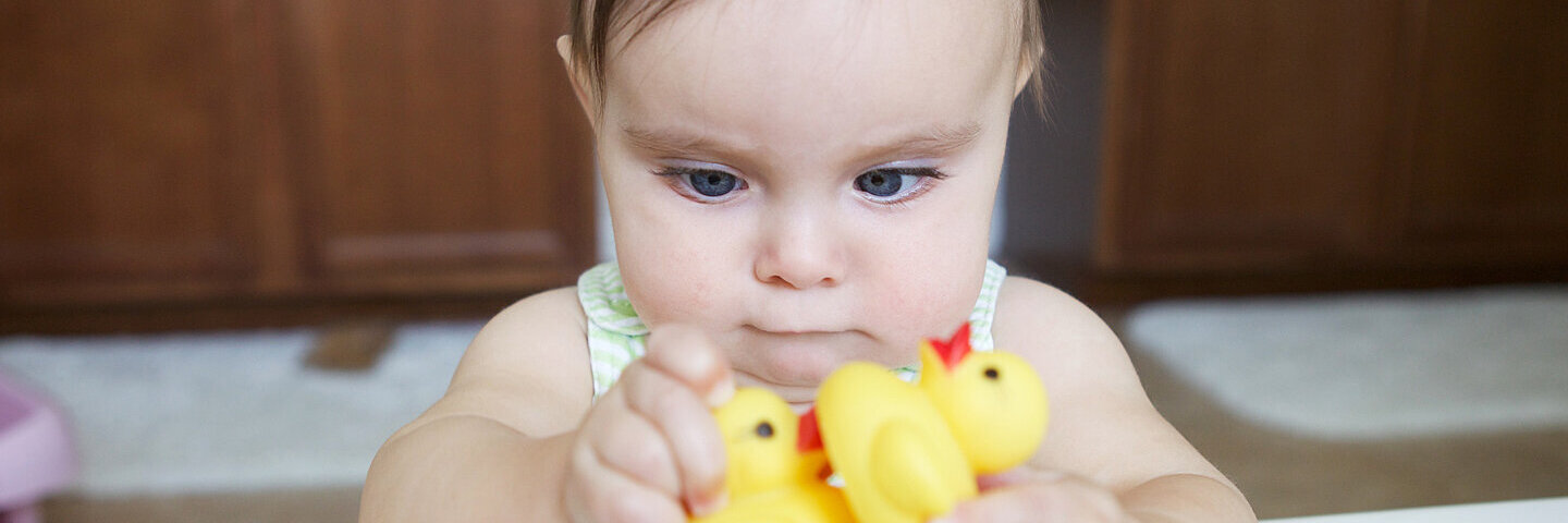 Ein Baby schielt und schaut zwei gelbe Gummienten an.