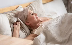Gesunder Schlaf im Alter: Frau liegt im Bett und genießt den Schlaf.