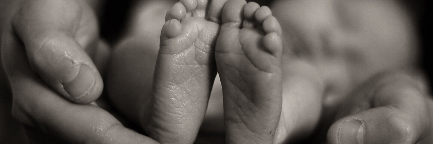Die Hände der Mutter halten die Füße ihres Sternenkindes.