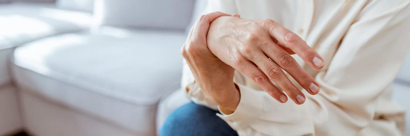Frau leidet durch ihre Fibromyalgie unter schmerzenden Gelenken und massiert ihre Hand.