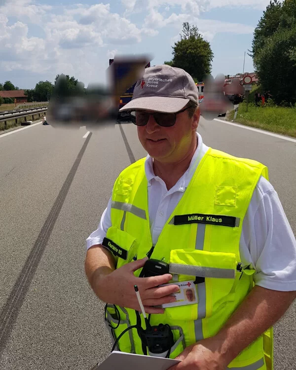 Klaus Müller vom Bayerischen Roten Kreuz steht mit einer Warnweste bei einem Einsatz auf der Landstraße.