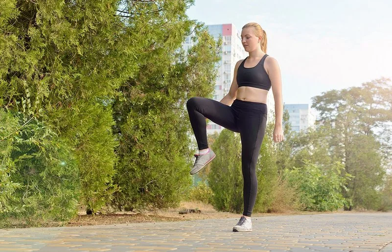 Eine Frau in Sportkleidung steht auf einem Bein und hält die Balance.