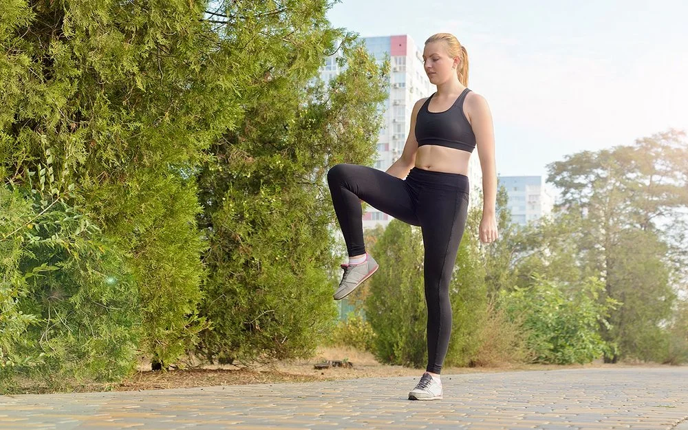 Eine Frau in Sportkleidung steht auf einem Bein und hält die Balance.