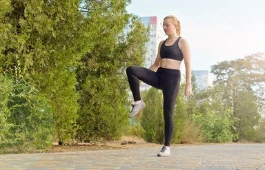 Eine Frau in Sportkleidung steht auf einem Bein und hält die Balance.