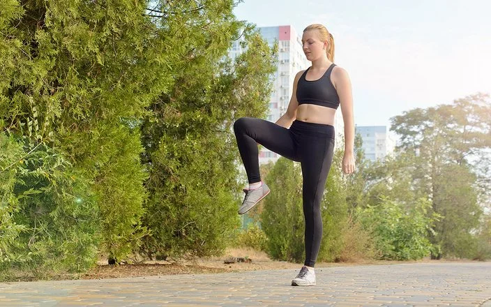 Eine Frau in Sportkleidung steht auf einem Bein und hält die Balance.