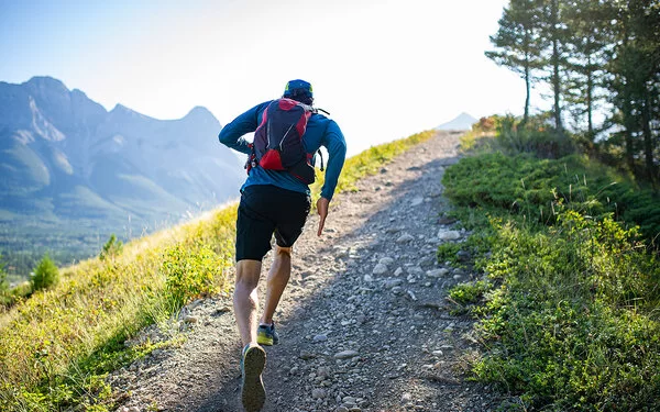 Ein Mann mit Rucksack läuft auf einem schmalen, steinigen Weg einen Berg herauf.
