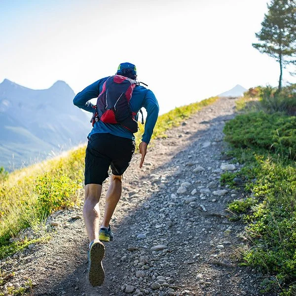 Ein Mann mit Rucksack läuft auf einem schmalen, steinigen Weg einen Berg herauf.