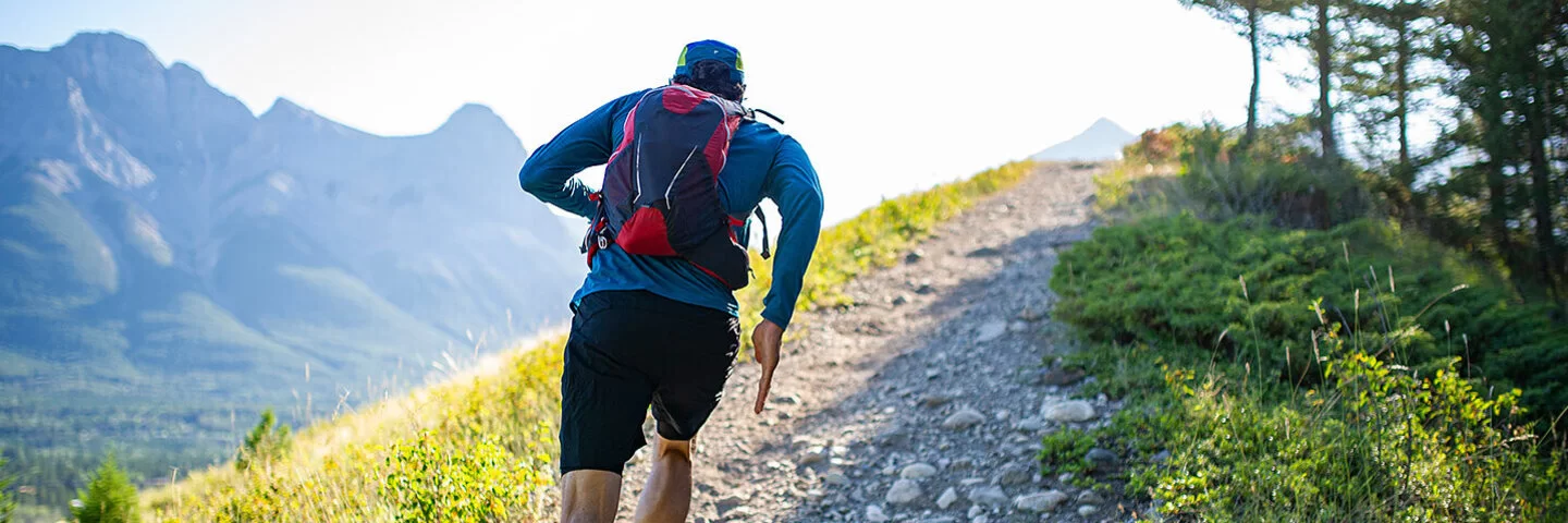 Ein Mann mit Rucksack läuft auf einem schmalen, steinigen Weg einen Berg herauf.