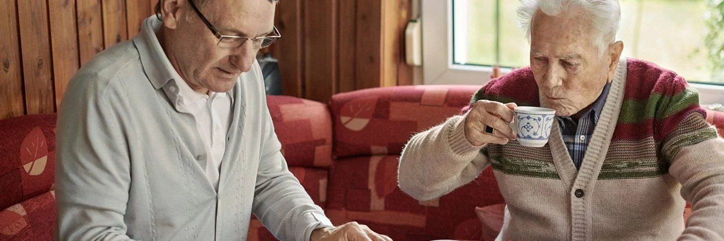 Sohn und älterer Vater sitzen am Küchentisch und planen Umbaumaßnahmen für barrierefreies Wohnen.