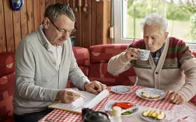 Sohn und älterer Vater sitzen am Küchentisch und planen Umbaumaßnahmen für barrierefreies Wohnen.