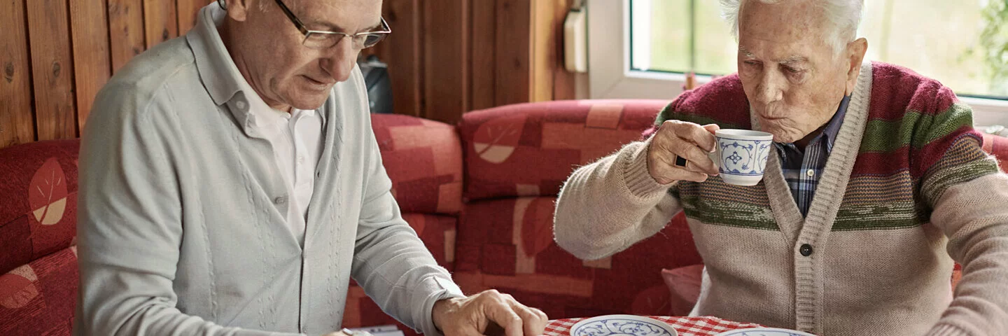 Sohn und älterer Vater sitzen am Küchentisch und planen Umbaumaßnahmen für barrierefreies Wohnen.