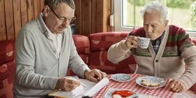 Sohn und älterer Vater sitzen am Küchentisch und planen Umbaumaßnahmen für barrierefreies Wohnen.