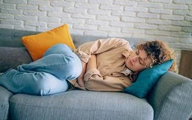 Eine junge Frau liegt auf dem Sofa und hat Endometriose-Beschwerden.