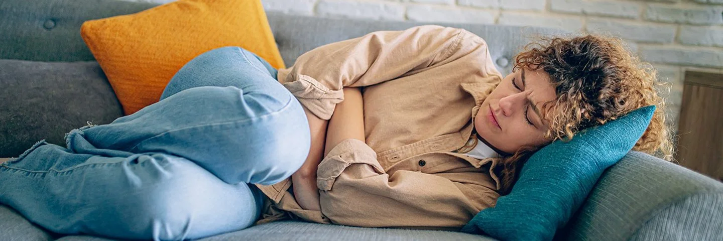 Eine junge Frau liegt auf dem Sofa und hat Endometriose-Beschwerden.