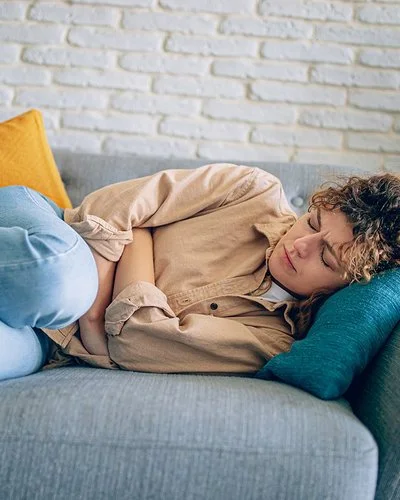 Eine junge Frau liegt auf dem Sofa und hat Endometriose-Beschwerden.